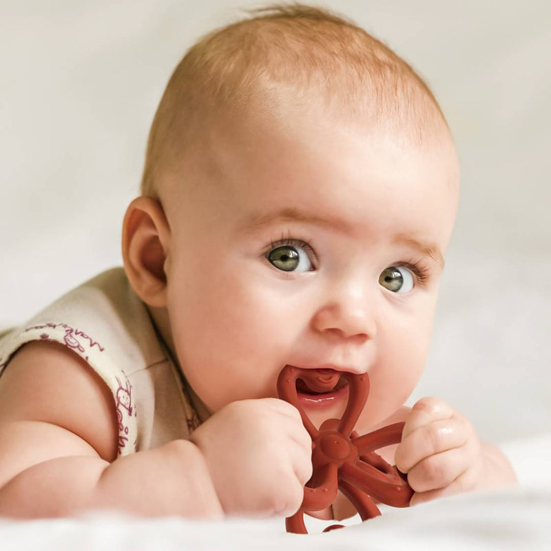 A baby chewing on a Haakaa Silicone Clover Teether to help ease sore gums and teething discomfort