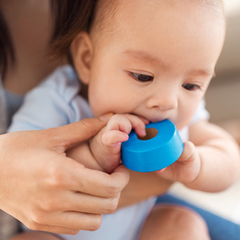 Baby chewing a round toy while being held by their mother