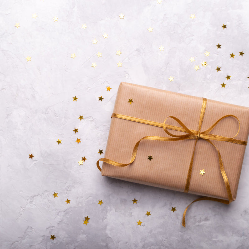 A gift wrapped in brown paper and gold ribbon. Gold stars are sprinkled over and around the gift.