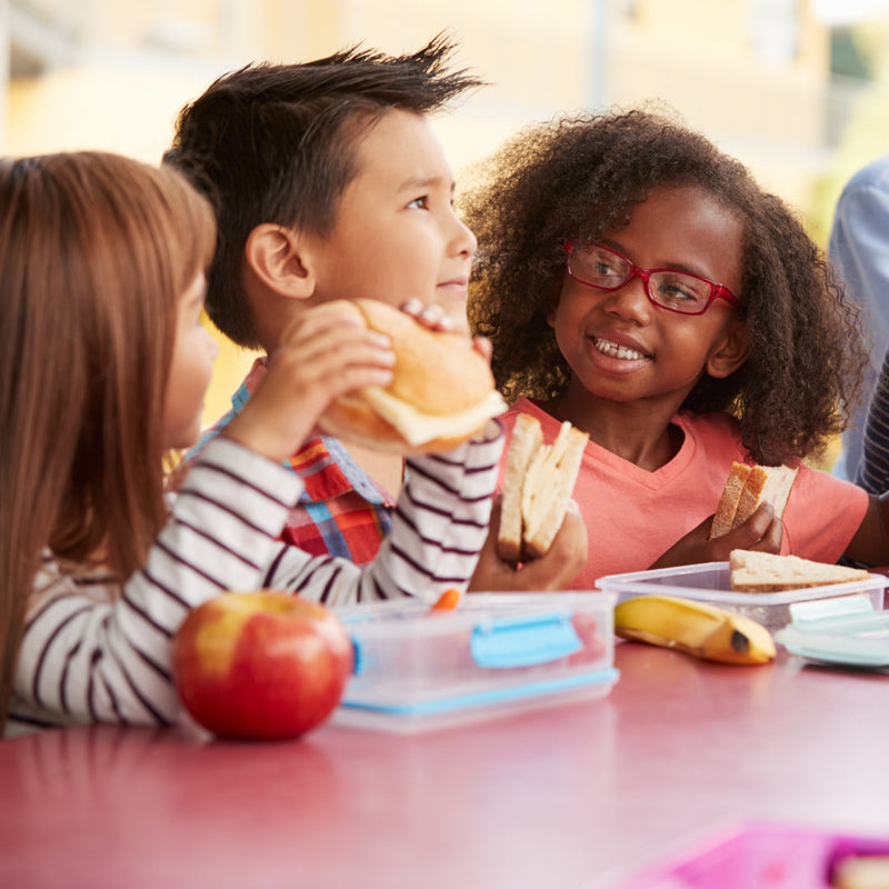 Three primary school aged children eating their school lunch at a table