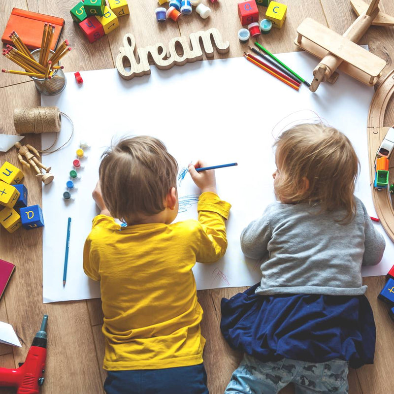 Overhead shot of toddlers lying on the floor and drawing on a large sheet of paper