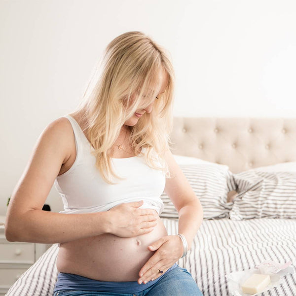A pregnant woman practicing self-care by gently massaging her belly with Haakaa Belly Bliss Lotion Balm