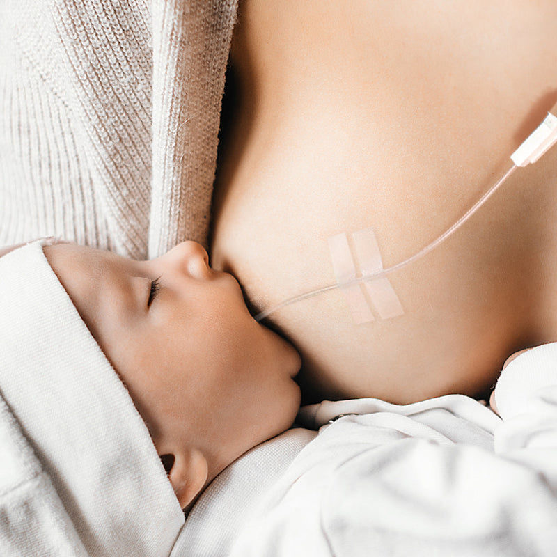 A baby breastfeeding while using a lactation aid/supplemental nursing system
